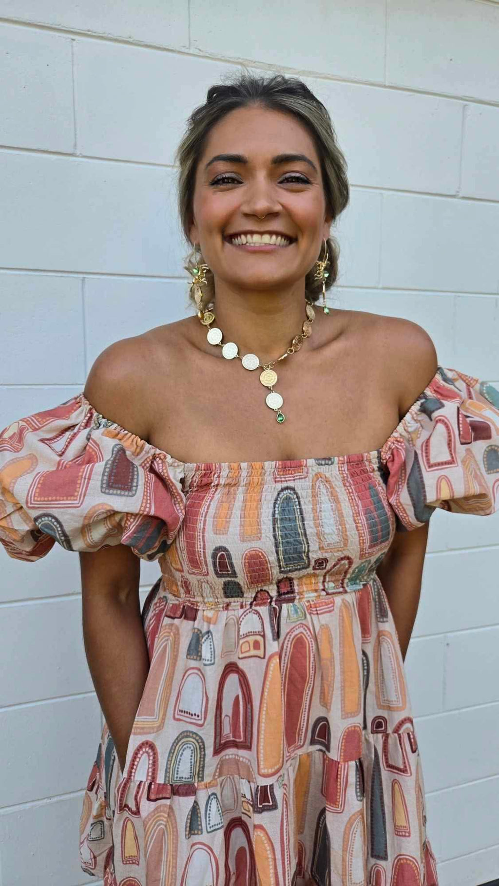 Woman wearing a colorful off-shoulder dress with a white tiled wall background