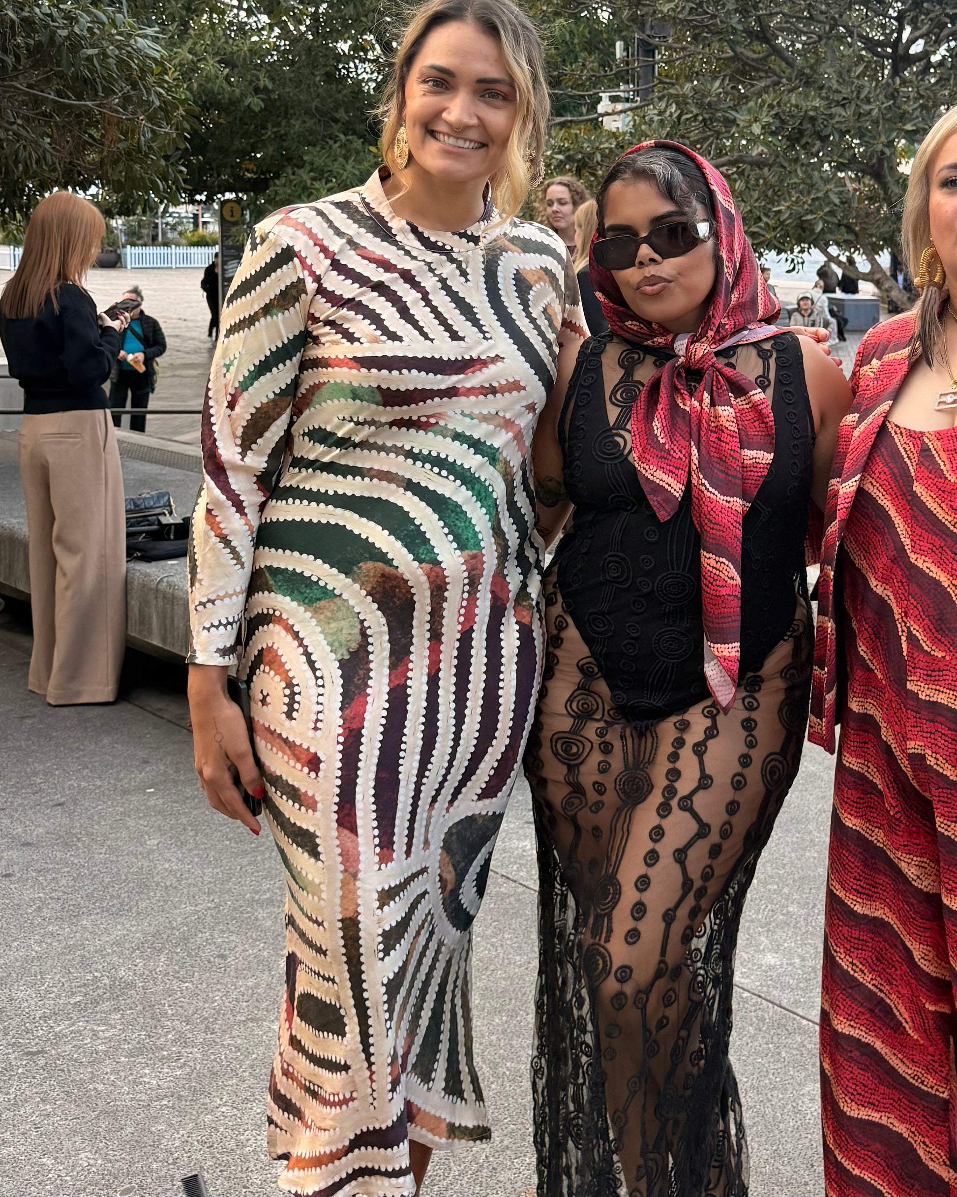 Two Aboriginal women posing outdoors, All wearing Aboriginal artwork clothing
