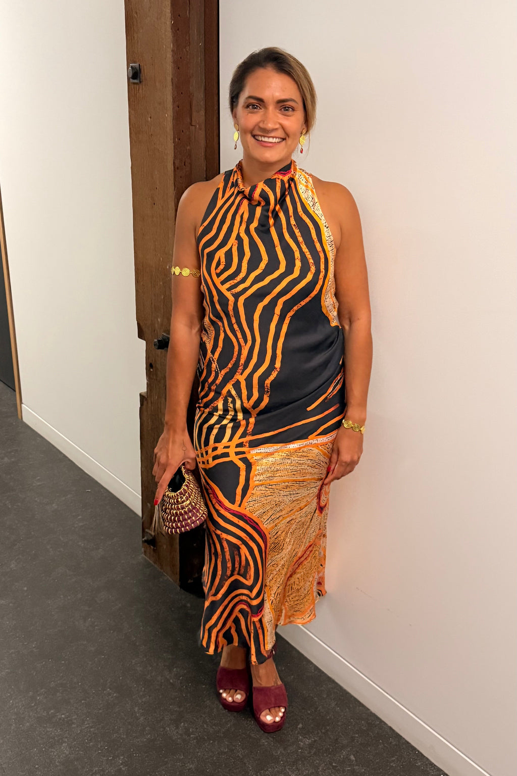 Aboriginal Woman in a First Nations designed dress standing against a white wall.