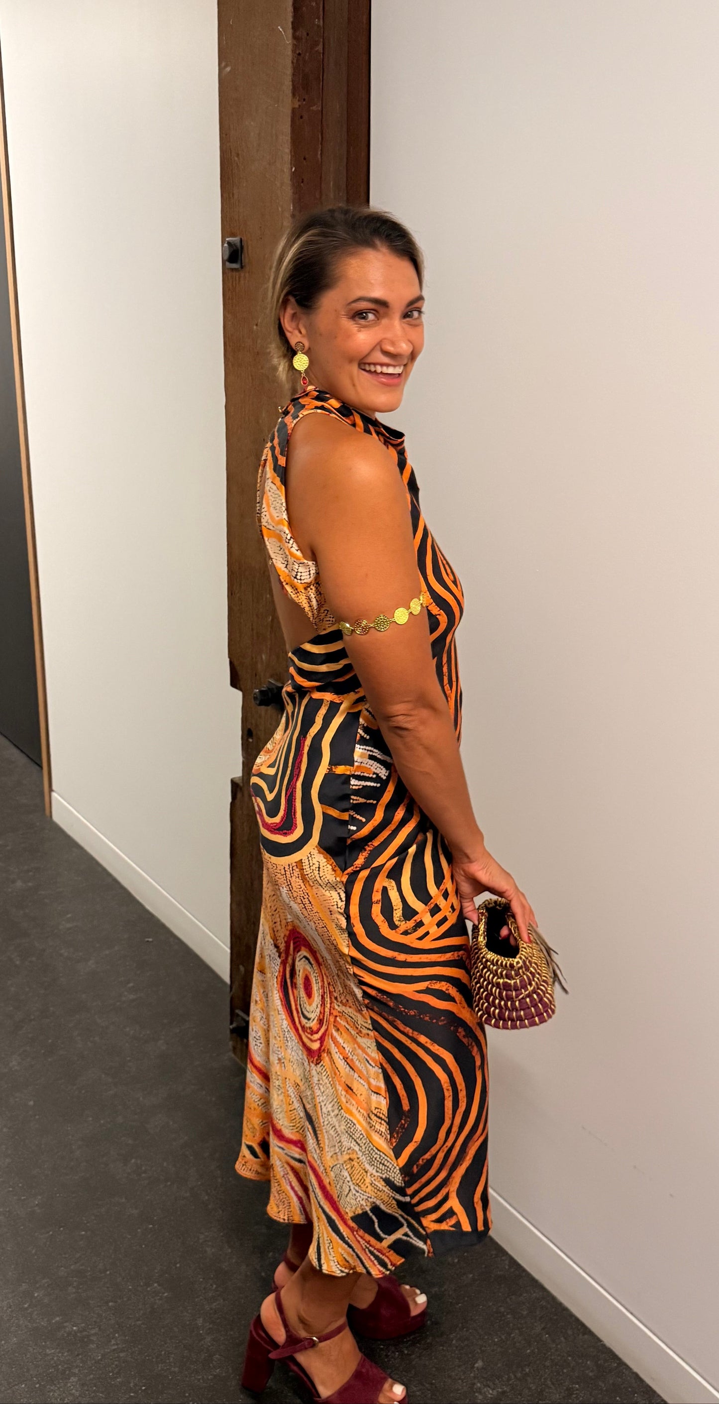 Aboriginal Woman in a First Nations designed dress standing against a white wall.
