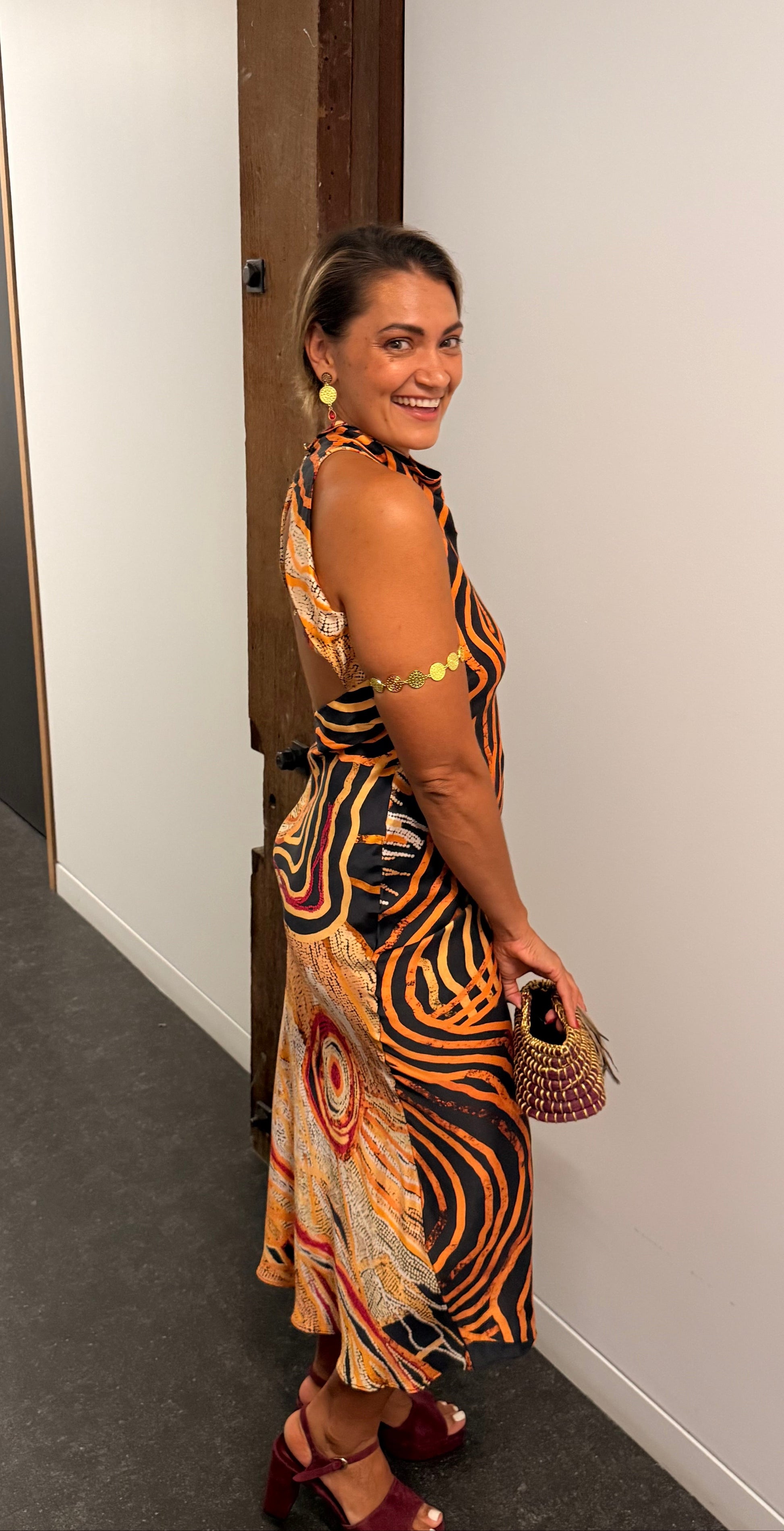 Aboriginal Woman in a First Nations designed dress standing against a white wall.