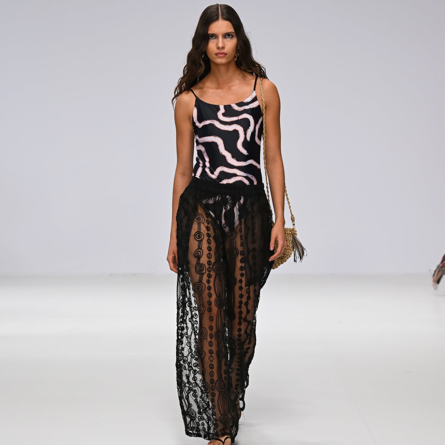 Model wearing Aborigina designed one piece bathers, with sheer black pants on a runway