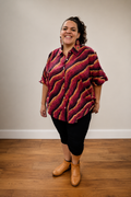 A Aboriginal woman wearing a button up sleeved top with reds and oranges Aboriginal art on it